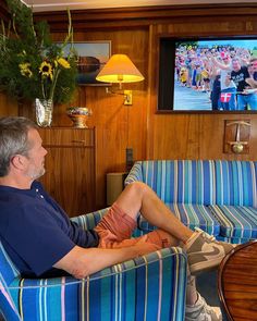 a man sitting in a blue striped chair and watching the football game on his tv