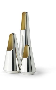 three silver vases sitting next to each other on a white surface with gold accents