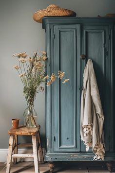 a blue armoire sitting next to a wooden stool and vase with flowers in it