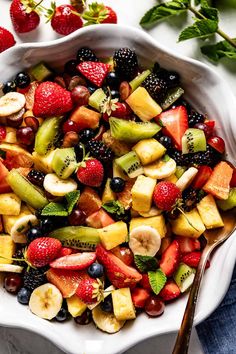 a white bowl filled with fruit salad next to strawberries