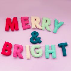 the word merry and bright spelled out in felt letters on a pink background with string