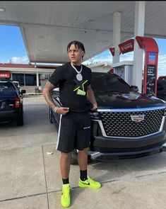 a man standing in front of a car at a gas station with his hands on his hips