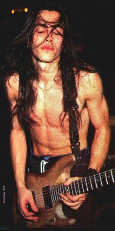 a shirtless man with long hair playing an electric guitar