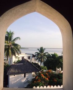 the view from an arched window looking out at water and palm trees in the distance