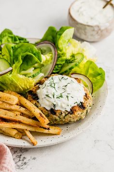 a white plate topped with french fries and a burger covered in ranch dressing next to lettuce