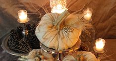 there are pumpkins and pine cones on the table with candles in front of them