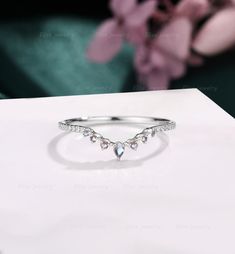 a diamond ring sitting on top of a white table next to a pink flower in the background