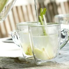 a pitcher pouring water into a cup filled with lemon slices and celery sticks