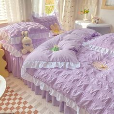 a bed room with two beds covered in purple comforters and stuffed animals on the pillows