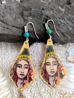 Literary Muse Earrings from our exclusive Artistry Adorned series. These earrings are a unique fusion of literature and art, designed to intrigue and inspire. Each piece was created from the original artwork which was hand-painted on a book page. The earrings are framed with a shimmering golden border. The design is completed with a vibrant teal bead, adding a pop of color and elegance. Key Features: Handcrafted Excellence: Each pair is meticulously crafted to ensure uniqueness and superior quality. Hand poured resin on wood. Artistic Design: Showcasing a hand-painted portrait on a book page, blending literary and artistic elements seamlessly. Elegant Border: The golden frame enhances the intricate artwork, making these earrings suitable for both casual and formal settings. Vibrant Accent: Book Page Earrings, Resin On Wood, Intricate Artwork, Original Canvas Art, Artistic Elements, Homemade Earrings, Golden Border, Golden Frame, Powerful Art