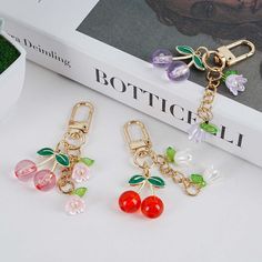 three charms with cherries hanging from them on a white table next to a book