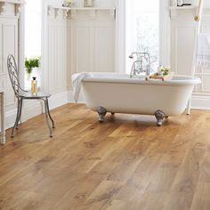 a bath tub sitting next to a window on top of a wooden floor in a bathroom