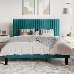 a bed with blue headboard and pillows in a white room next to two pictures on the wall