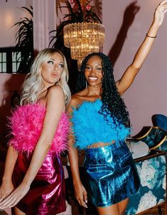 two beautiful women standing next to each other in front of a chandelier hanging from the ceiling