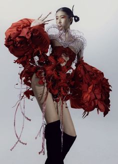 a woman in red dress and black boots posing with her hands on her hips while holding flowers