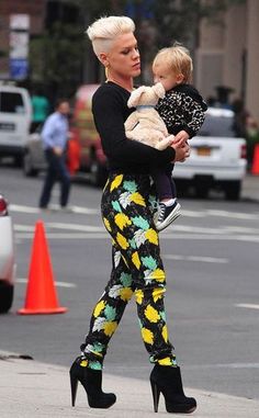 a woman walking down the street holding a baby in her arms and wearing high heeled shoes