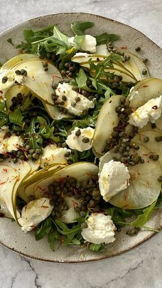 a white plate topped with sliced pears and capers on top of a marble table