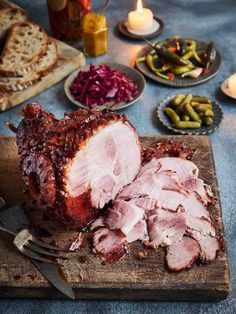 sliced ham on a cutting board with pickles, bread and candles in the background