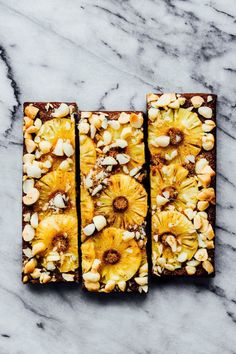 two pieces of cake with pineapples and nuts on top sitting on a marble surface