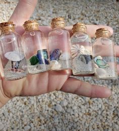 small bottles filled with different types of sea shells and sand in them, sitting on a person's hand