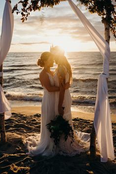 two brides kissing under an arch on the beach