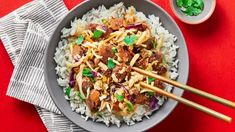 a bowl filled with rice, meat and veggies on top of a red table