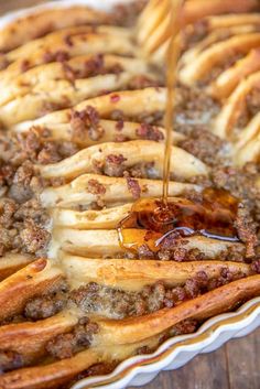 someone is pouring syrup on some food in a pie pan with french fries and other toppings