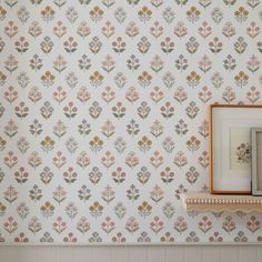 the wall paper has flowers on it and is next to a shelf with a framed photo