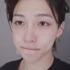 a close up of a person wearing a black shirt and silver earrings, looking at the camera