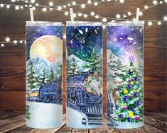 three travel mugs decorated with christmas scenes and lights on a wooden table in front of a wood paneled wall