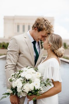 a bride and groom standing next to each other in front of a fountain with white flowers