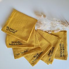 five yellow napkins with words on them sitting next to some dried grass and white flowers