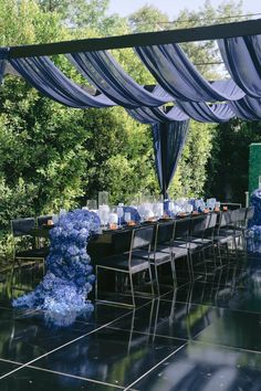 an outdoor dining area with blue and white flowers on the table, chairs and canopy