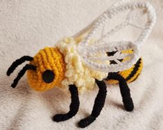 a small crocheted bee sitting on top of a white blanket next to a black and yellow object