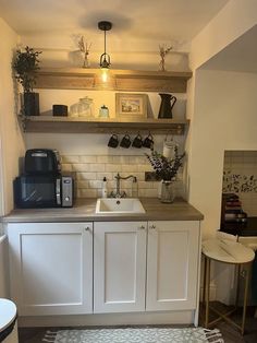 a small kitchen with white cabinets and wooden shelves above the sink, along with an area rug on the floor