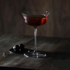 a glass filled with liquid sitting on top of a wooden table next to an olive