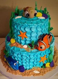 a birthday cake with an ocean theme and fish on the bottom tier is decorated in blue icing