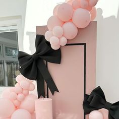 pink and black balloons are on display in front of a building with a large balloon arch