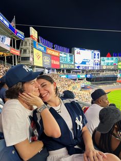 two women are sitting in the stands at a baseball game and one is hugging her face