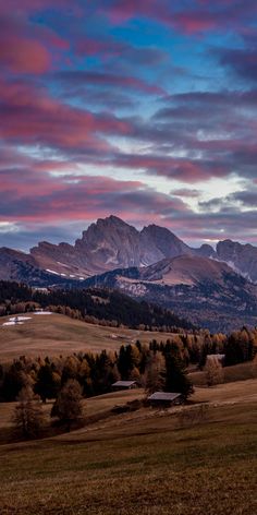 the mountains are covered in snow and clouds as the sun is setting over them on a cloudy day