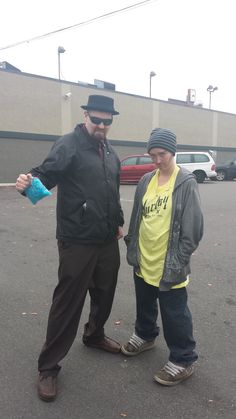 two people standing in the middle of a parking lot with cars behind them and one person wearing a hat