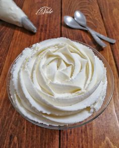 a glass bowl filled with whipped cream on top of a wooden table next to spoons