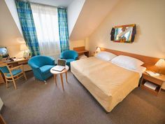 a bed room with a neatly made bed and two chairs next to a desk in front of a window