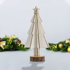 a paper christmas tree on a wooden base surrounded by evergreen branches and gold baubles