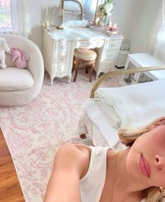 a woman laying on top of a bed next to a white chair and desk in a bedroom