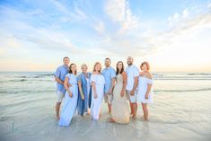 a group of people standing on top of a beach next to the ocean at sunset