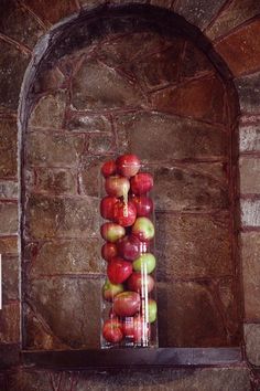 a tall glass vase filled with red and green apples sitting on top of a shelf