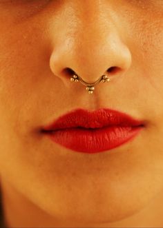 a woman's nose with a gold nose ring attached to her nose and red lipstick