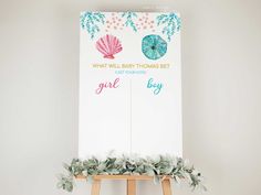 a baby shower sign on a easel with greenery and shells painted on it