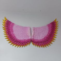 a pink and yellow paper sculpture on a white wall with an open wing like design